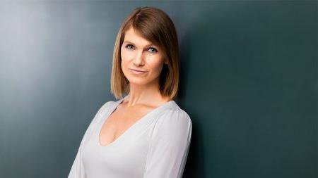 Lauren Schultes wearing white shirt posing against dark green background.