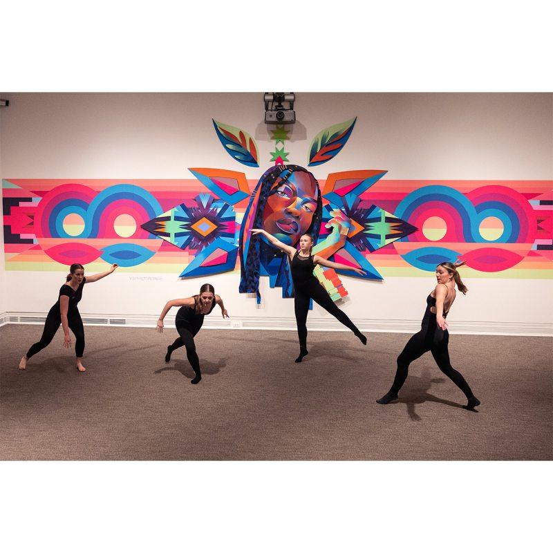 Dancers dancing in front of a large tapestry art display.